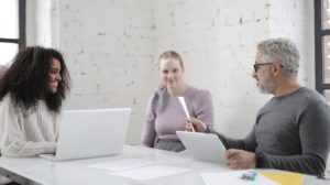 Three people sitting in a white brick walled office with computers