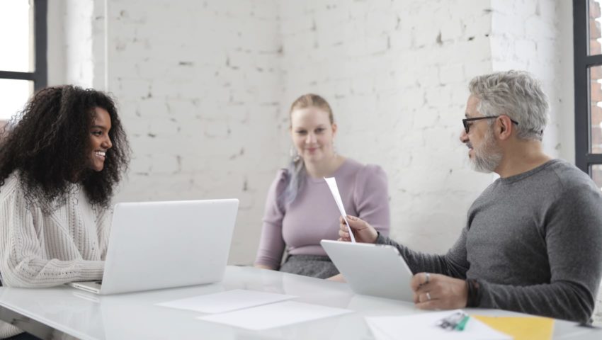 Three people sitting in a white brick walled office with computers