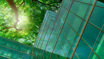 Eco-friendly building in the modern city. Green tree branches with leaves and sustainable glass building for reducing heat and carbon dioxide. Office building with green environment