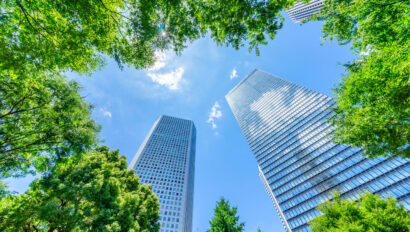 looking up view of panoramic modern city skyline with blue sky and green tree