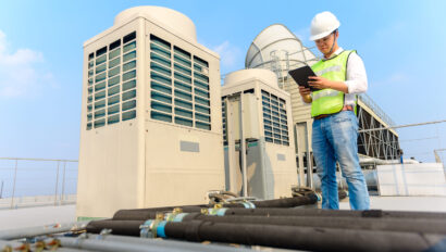 Engineer holding tablet is checking the cooling tower on the roof of the building to be in good condition.