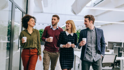 Group of diverse coworkers walking through a corridor in an office, holding paper cups