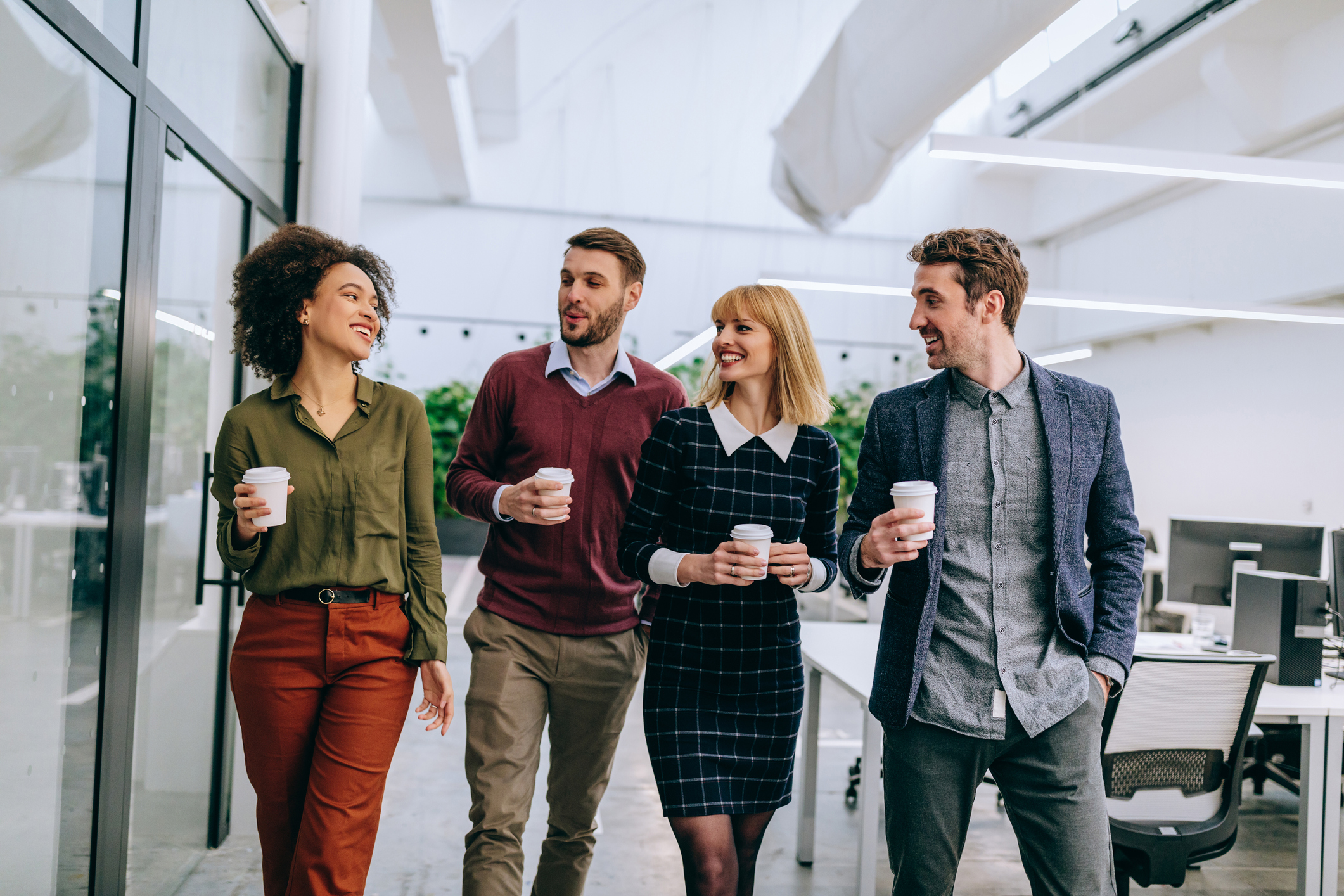 Group of diverse coworkers walking through a corridor in an office, holding paper cups