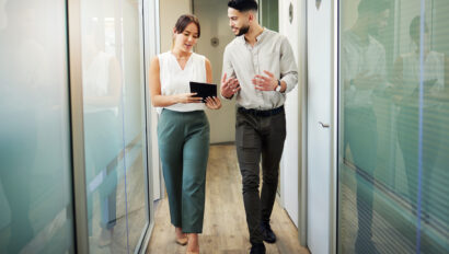 Full length shot of two young businesspeople walking through the office and having a discussion about today's proptech landscape while using a digital tablet.