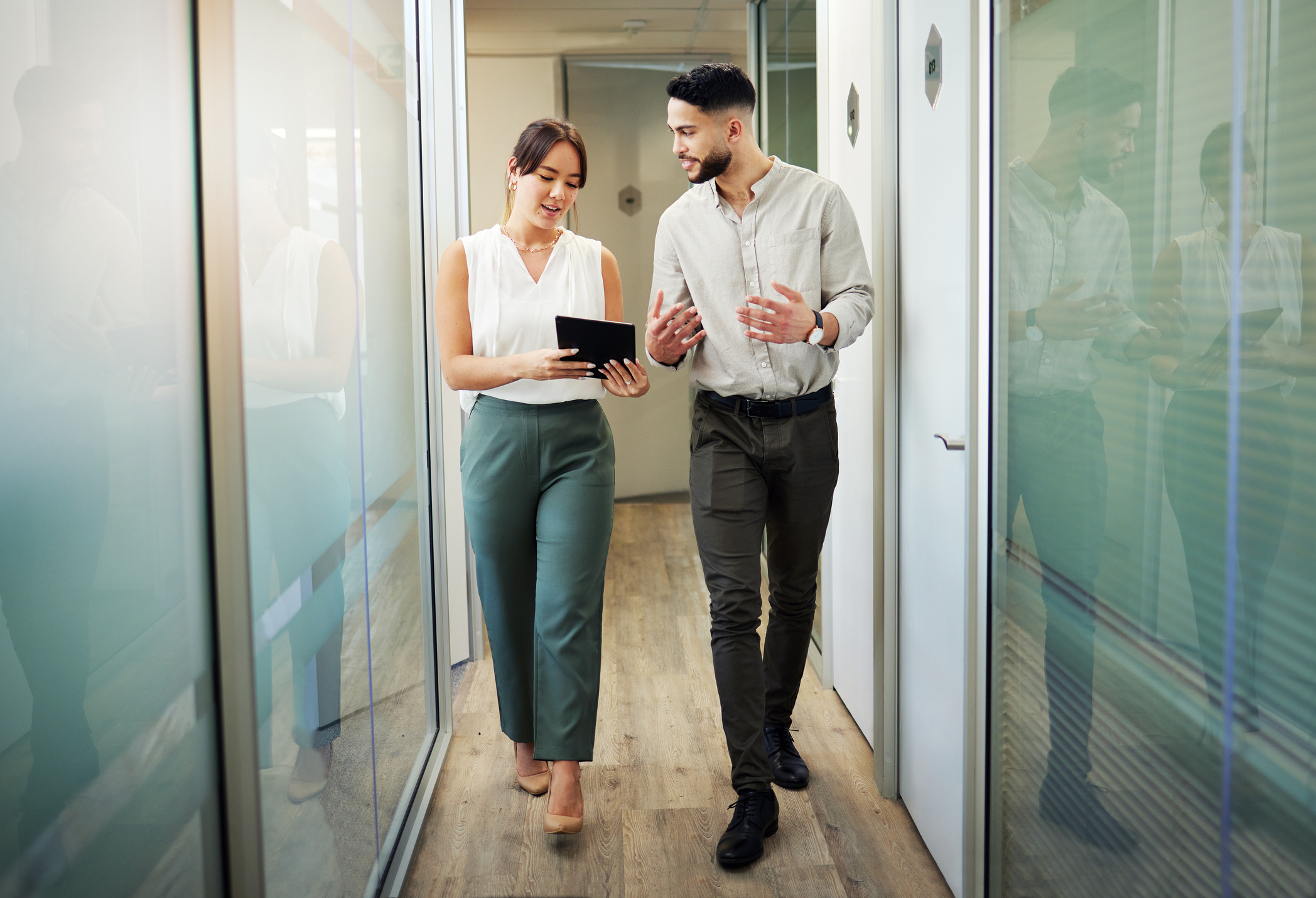 Full length shot of two young businesspeople walking through the office and having a discussion about today's proptech landscape while using a digital tablet.
