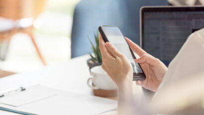 Female hand using smartphone while working at desk in office