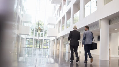 Rear View Of Businessmen Walking Through Office Lobby
