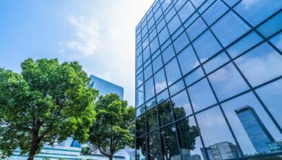 trees and blue sky reflected on the glass wall