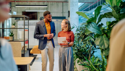 Two managers walking through a modern green office, discussing project details while using a tablet in a bright, airy workspace
