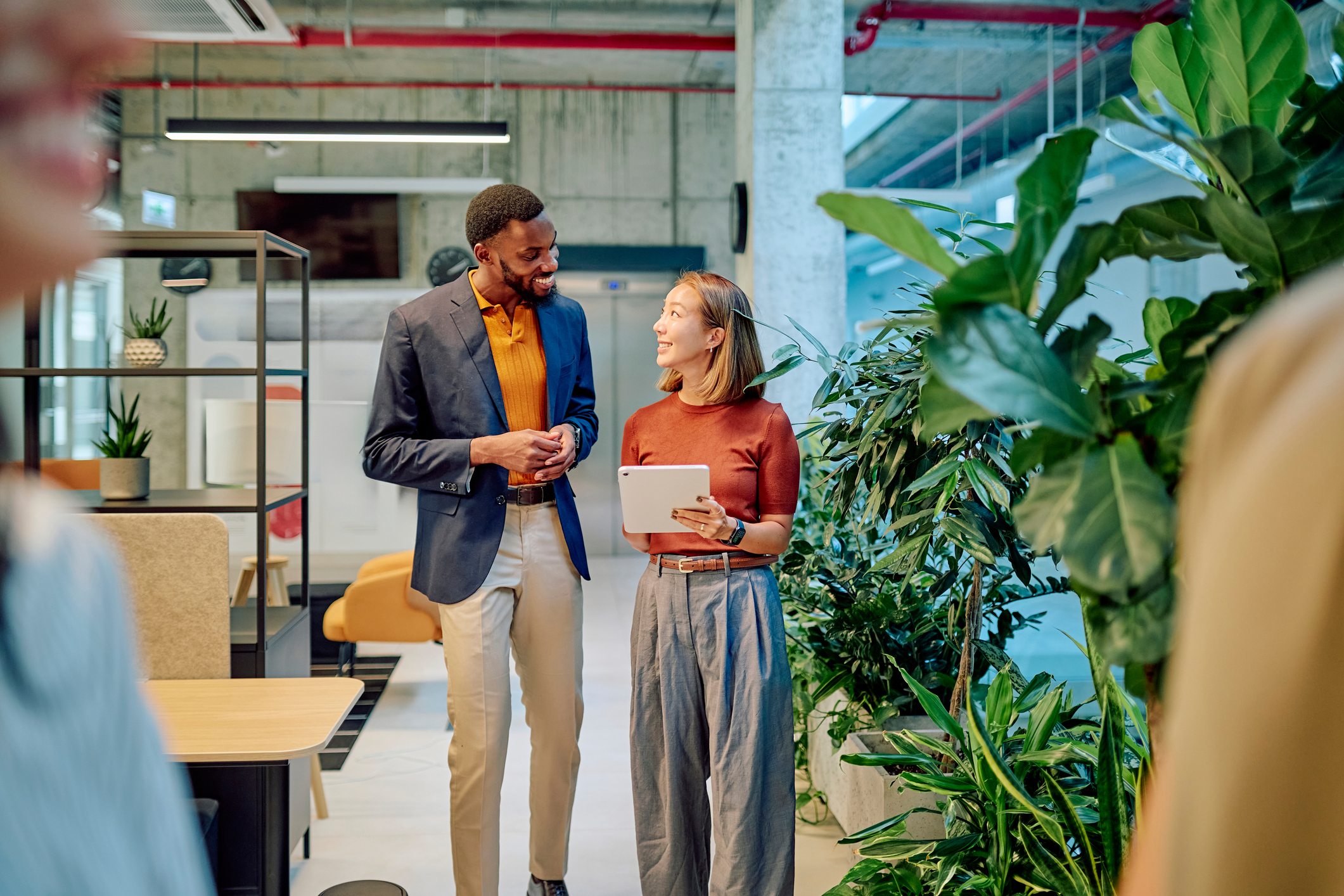 Two managers walking through a modern green office, discussing project details while using a tablet in a bright, airy workspace